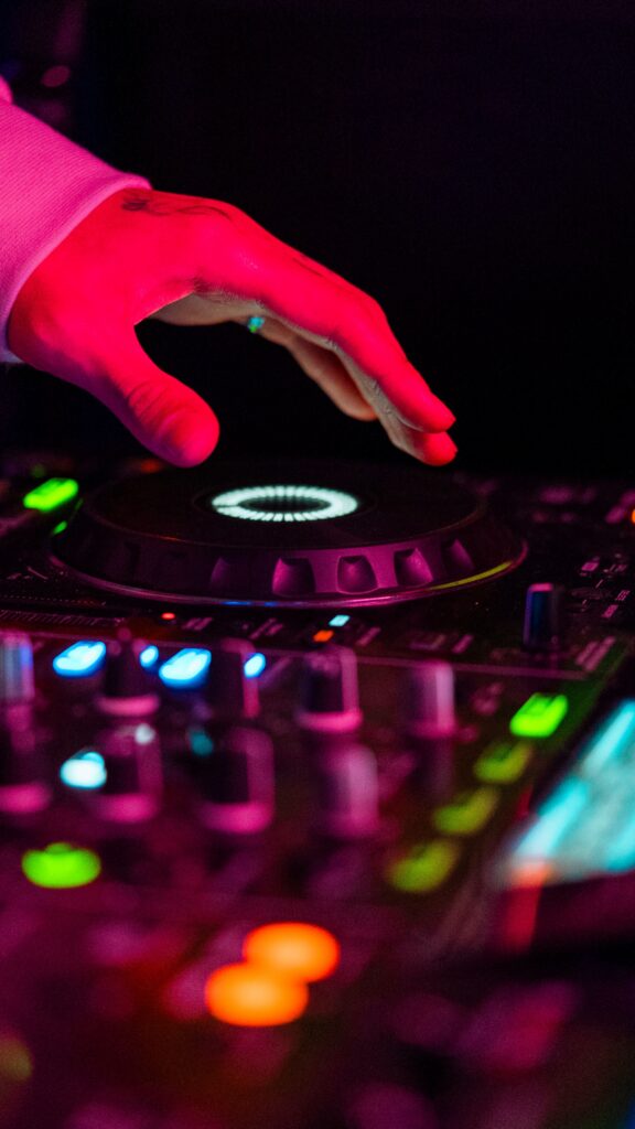 Close-up of a DJ's hand mixing music in a vibrant club setting under colorful lights.