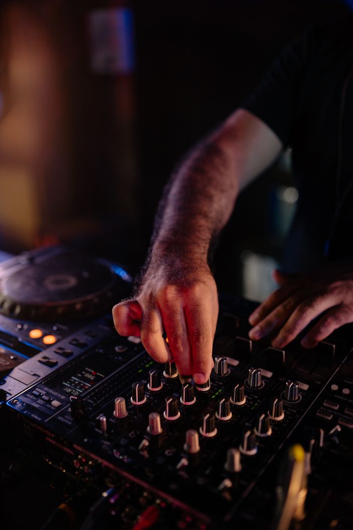 Close-up of a DJ's hands adjusting an audio mixer in a dimly lit club scene.